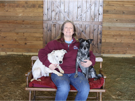 A woman seated on a chair, accompanied by two dogs, enjoying a moment of companionship and relaxation.