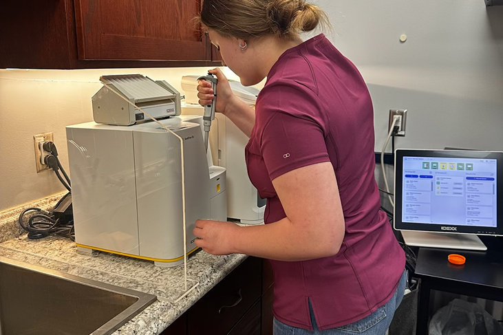 A woman wearing a purple shirt operates a machine, focused on her task in a well-lit environment.