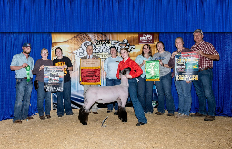 A group of people proudly holding their sheep at a livestock show, showcasing their animals to the audience.